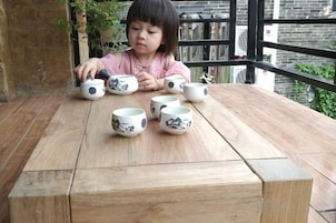 Un niño sentado a una mesa de madera con varias tazas de cerámica.