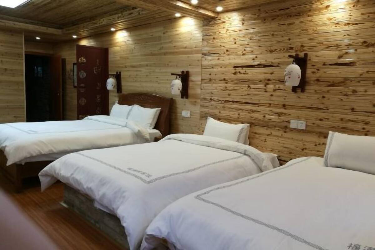 A room with wooden walls, two beds with white bedding, and a wooden ceiling with recessed lighting.