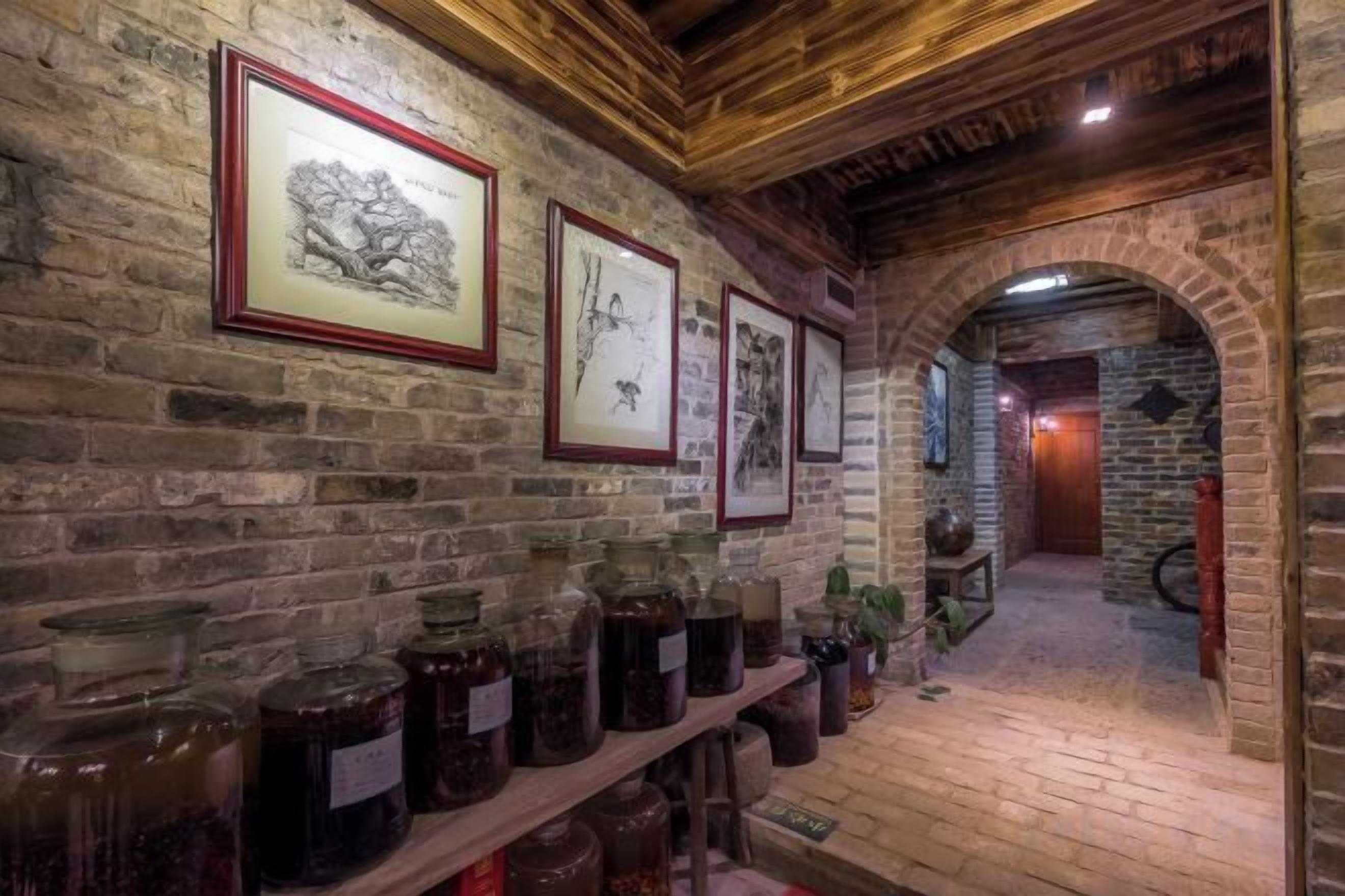 A brick corridor with framed pictures on the walls and shelves of jars.