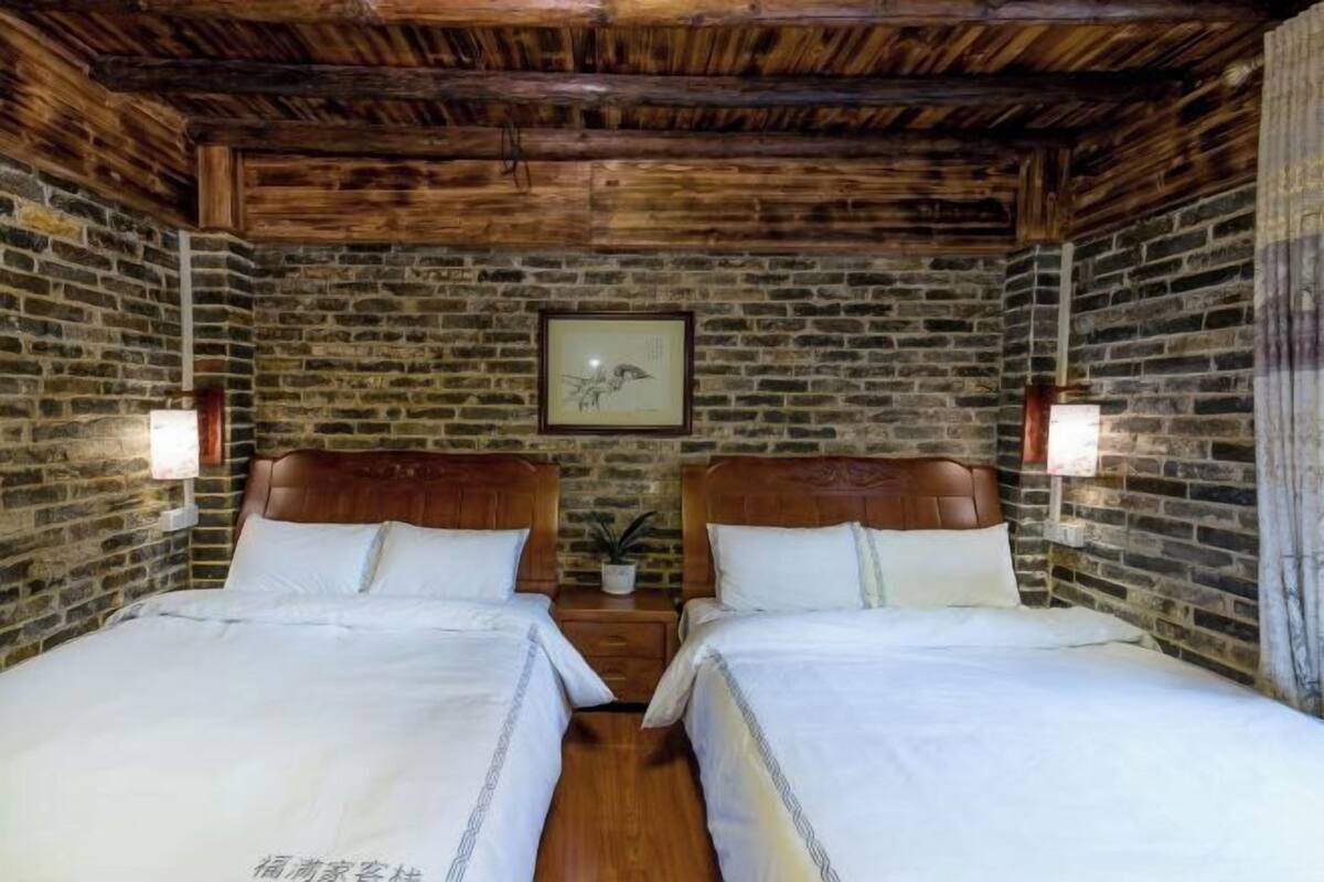 A room with two beds, wooden beams on the ceiling, brick walls, and a framed picture on the wall.
