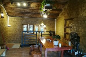 A rustic interior with a wooden dining table, chairs, a hanging plant, and a stone wall. - Fu Man Jia Ke Zhan (Zhaoping)