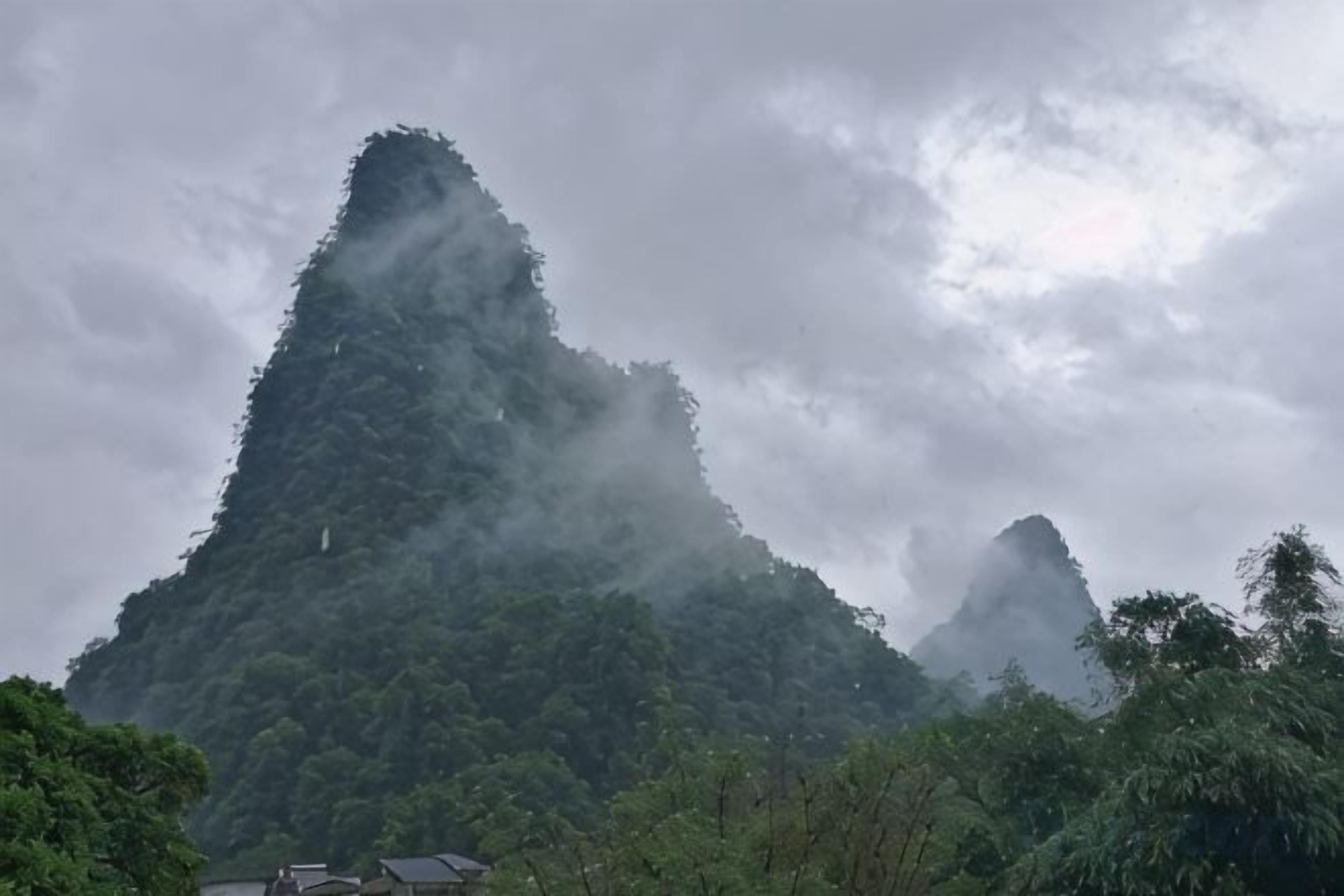 A mountain with a peak shrouded in mist, surrounded by dense forest.