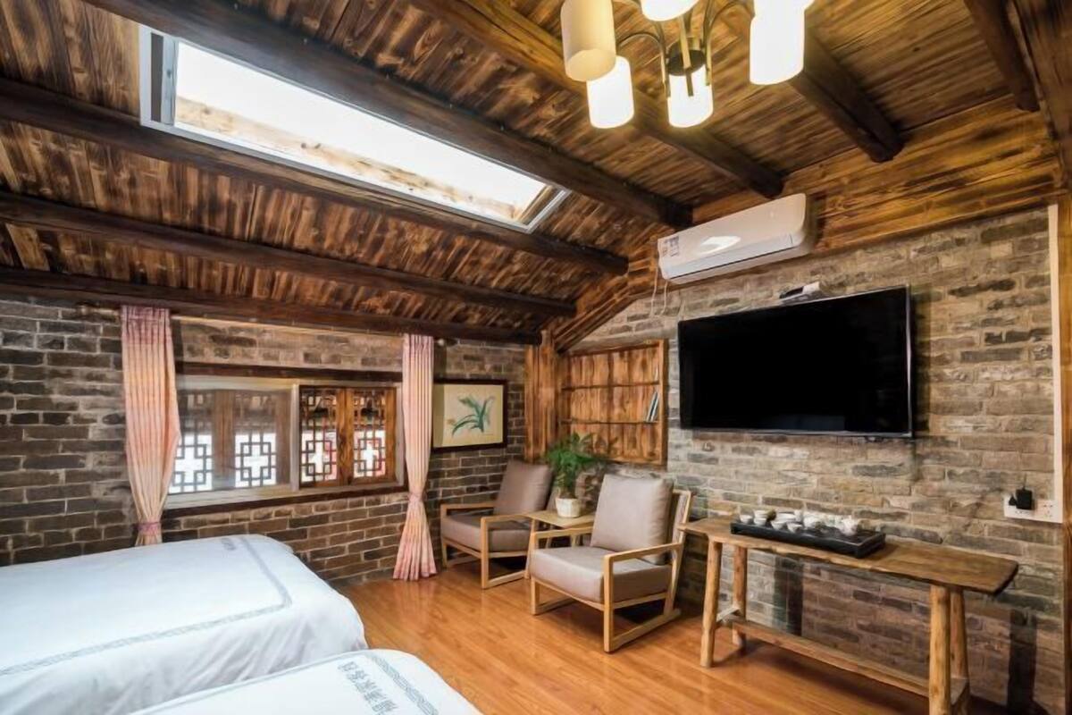 A rustic room with a wooden ceiling, brick walls, a TV, a bed, and a seating area.
