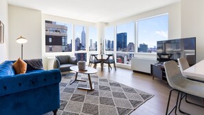 Un salon moderne avec vue sur la ville, un canapé bleu, une table à manger et un téléviseur.