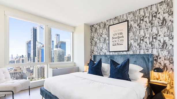 Une chambre d’hôtel moderne avec un grand lit, une vue sur la ville et une citation encadrée accrochée au mur.