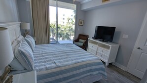 Habitación de hotel con cama, televisor, ventilador de techo y vistas al exterior.