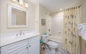 A bathroom with a white sink, mirror, toilet, and shower curtain.