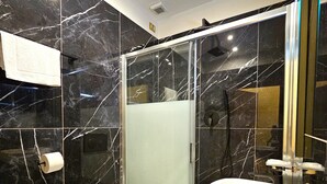 Un bagno moderno con bidet, toilette e lavandino, il tutto caratterizzato da pareti in marmo e un box doccia in vetro.