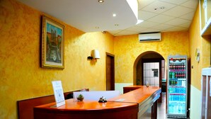 Una reception con un quadro incorniciato sopra, un faretto a parete e una macchina distributrice di bevande.