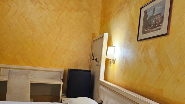 Una camera d'albergo con un letto, un condizionatore, un comodino, una lampada e un quadro appeso al muro.