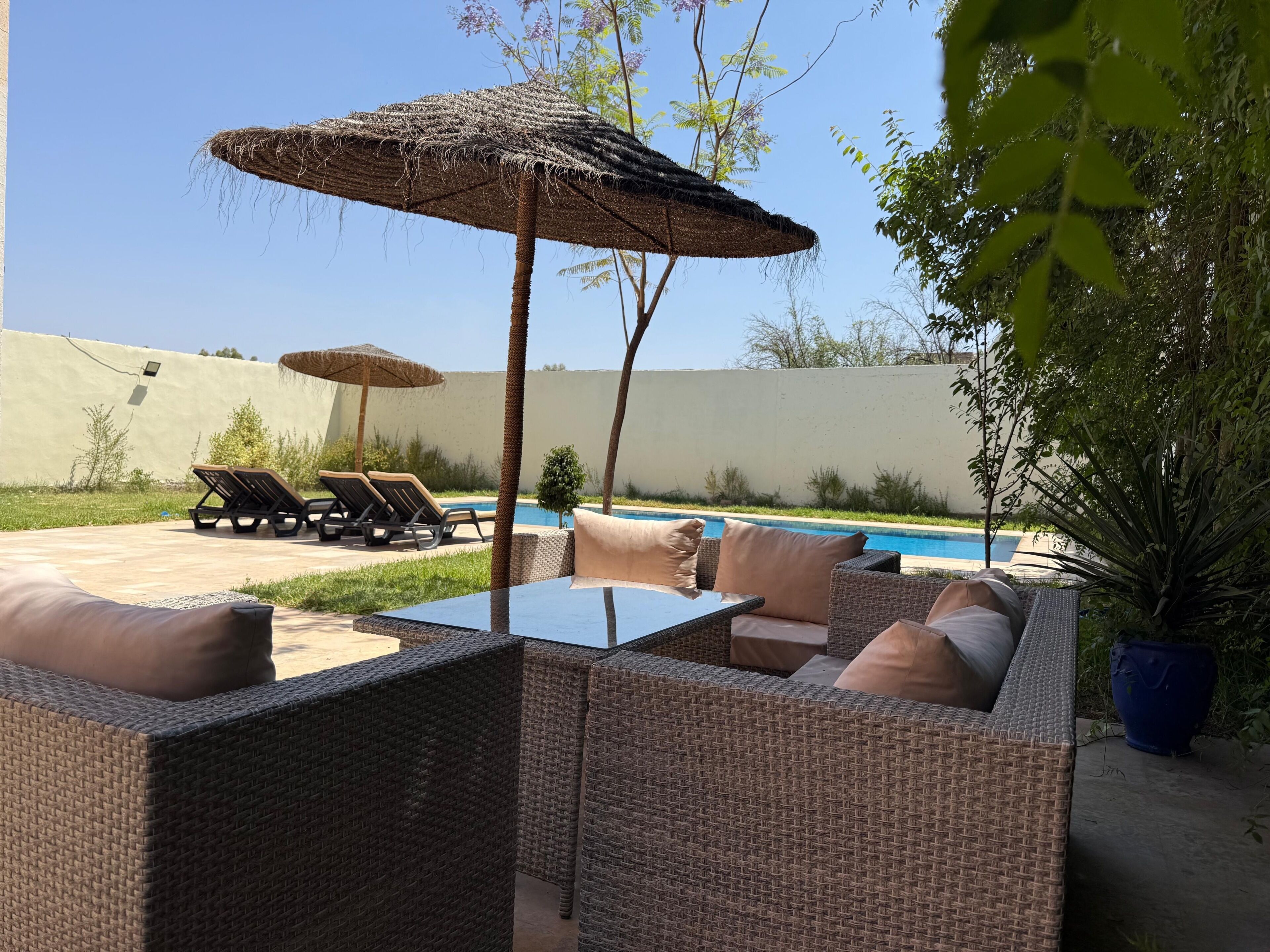 A patio area with wicker furniture, a pool, and a thatched umbrella.