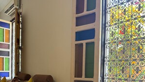 A room with a sofa, patterned cushions, a window with decorative iron bars, and an air conditioning unit.