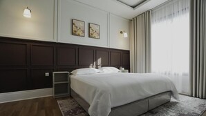 A modern bedroom with a large bed, a nightstand, a side table, and a wall-mounted lamp. - Nma'a Residences (Riyadh)