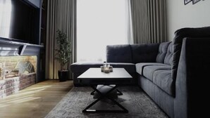 A modern living room with a dark blue accent wall, a fireplace, a grey sofa, and a coffee table. - Nma'a Residences (Riyadh)