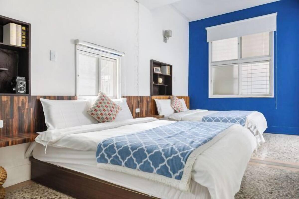 Habitación de hotel con dos camas, una pared azul de acento y una ventana con persianas.