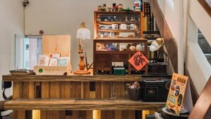 A wooden reception desk with a lamp, a bookshelf with various items, and a sign with Chinese characters. - We Share Hostel (Tainan)
