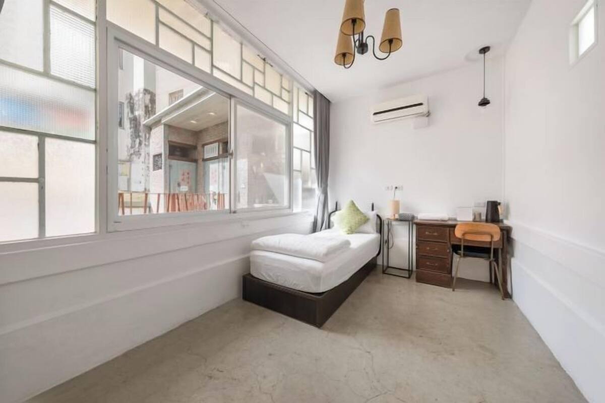 Un dormitorio moderno con cama, escritorio y silla, ventanas amplias y un equipo de aire acondicionado.