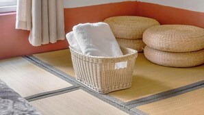 A corner of a room with a woven basket containing a white towel, a woven ottoman, and a woven stool. - We Share Hostel (Tainan)