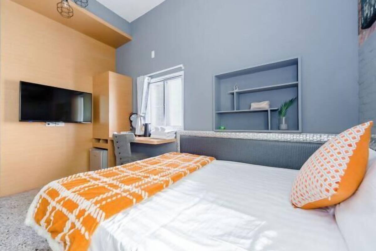 Una habitación de hotel moderna con cama, escritorio, televisor y ventana.