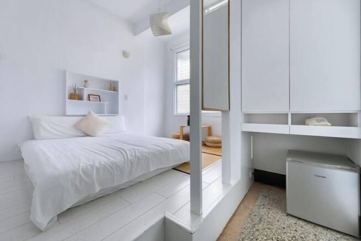 Un dormitorio moderno con cama, paredes blancas, armario empotrado y una pequeña mesa con lámpara.