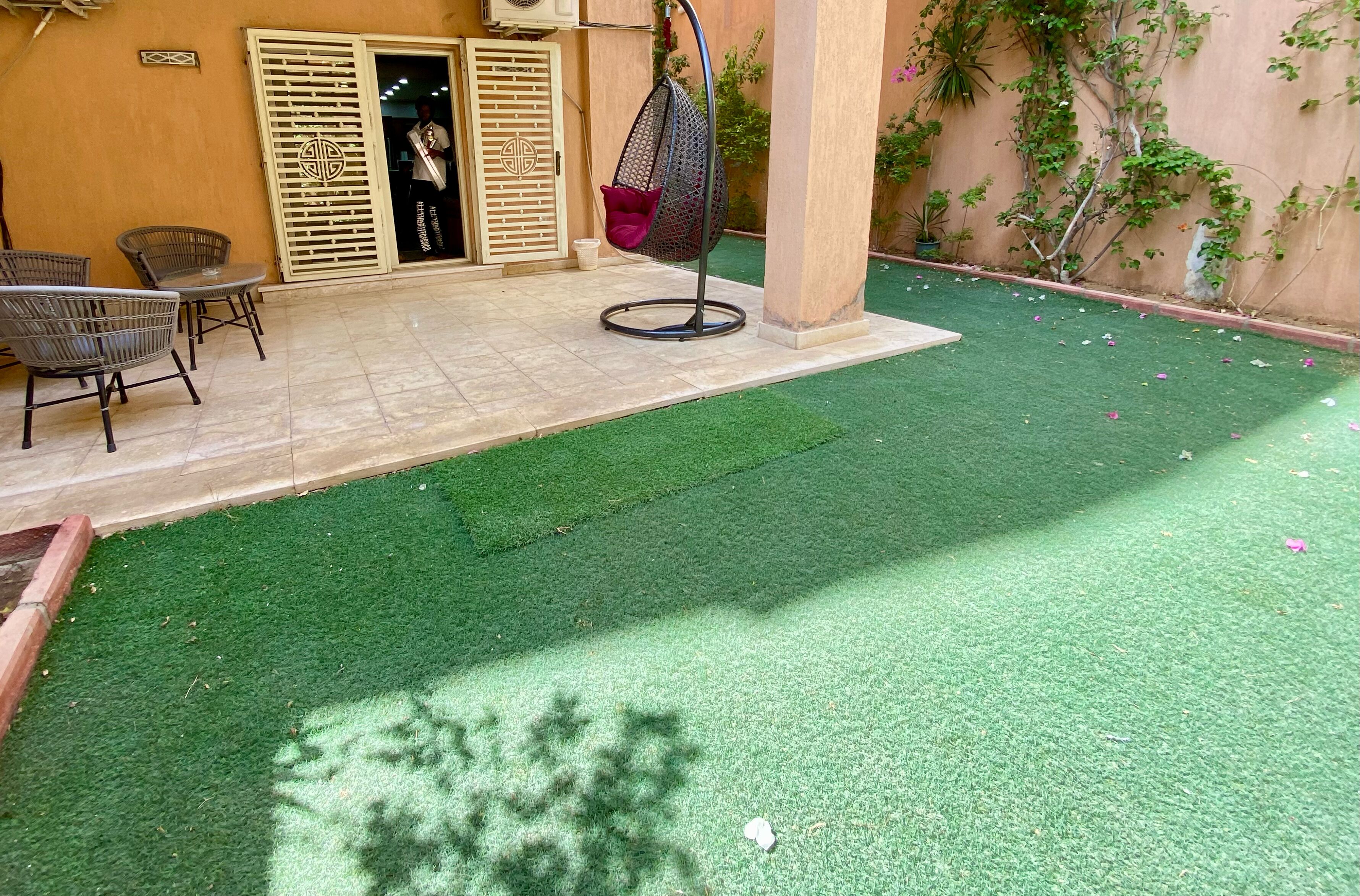 Un área de patio con césped artificial, una silla colgante y una mesa.