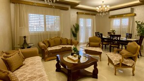 A spacious living room with a large sofa set, a coffee table, and a dining area with chairs and a table. - Luxurious Villa Serene Garden New Cairo (New Cairo)