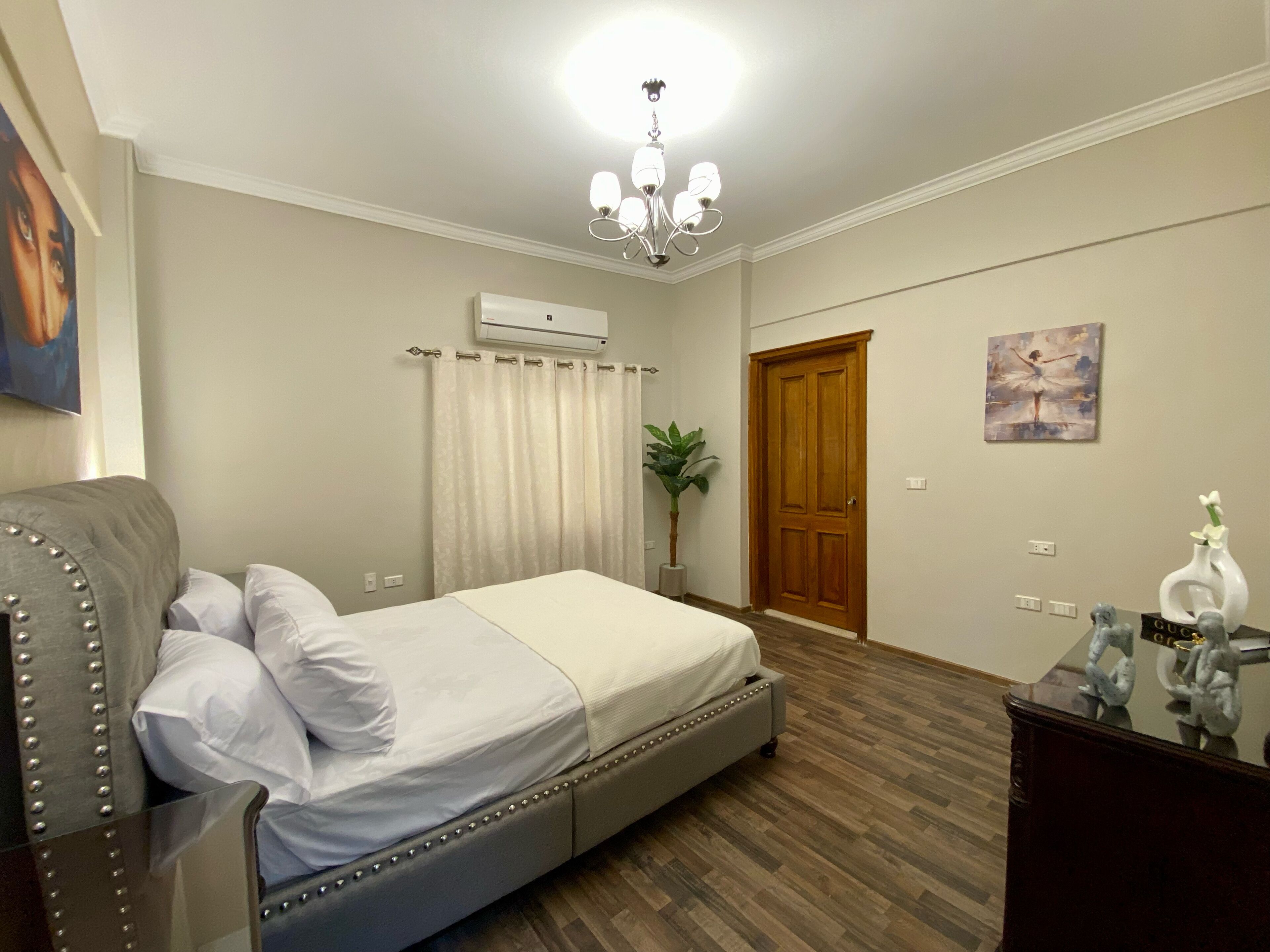 A bedroom with a bed, a bedside table, a chair, a wooden door, and a ceiling light.