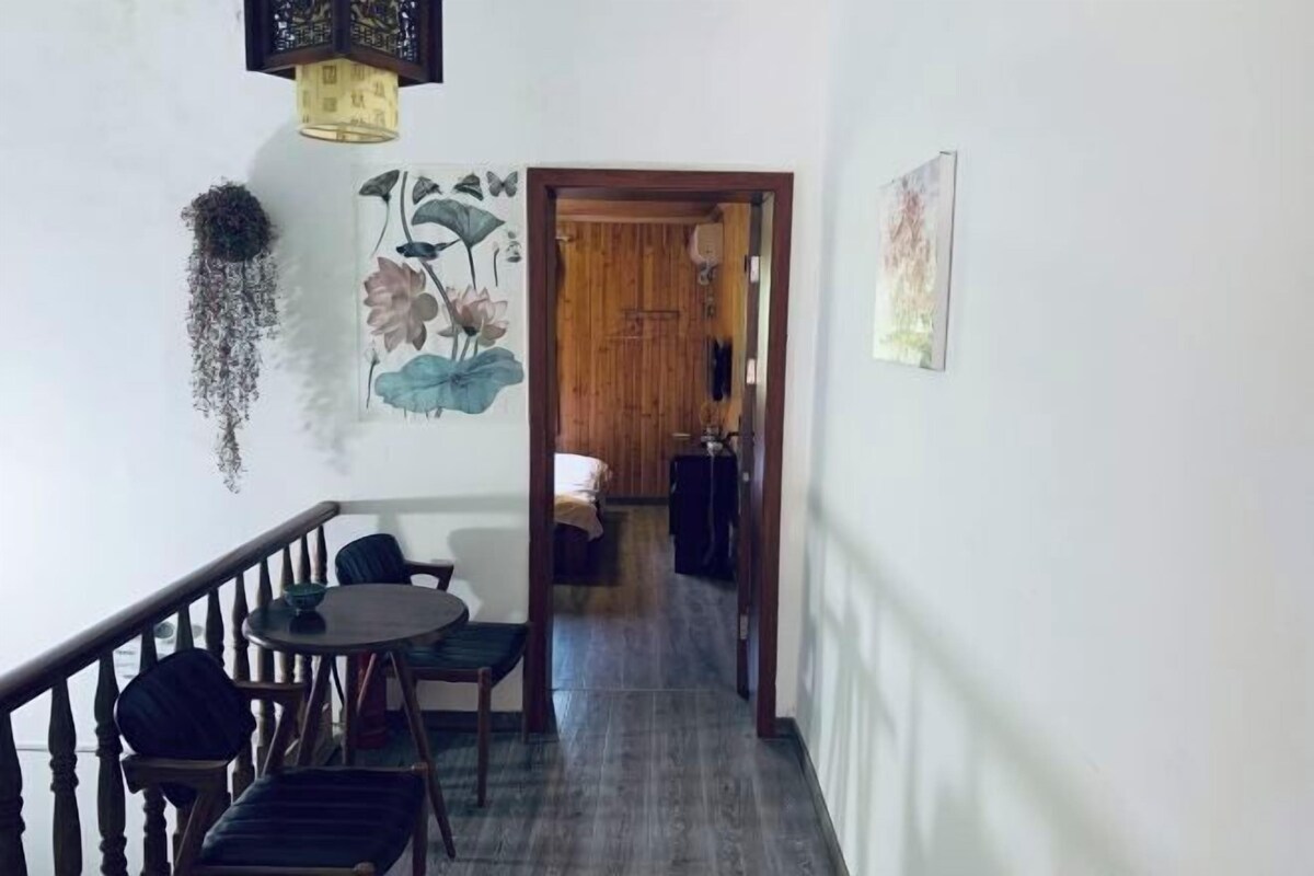 A hallway with a staircase, a dining area with chairs and a table, and a wooden door leading to another room.