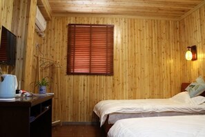 A room with wooden walls, a bed, a bedside table with a lamp, and a window with blinds.