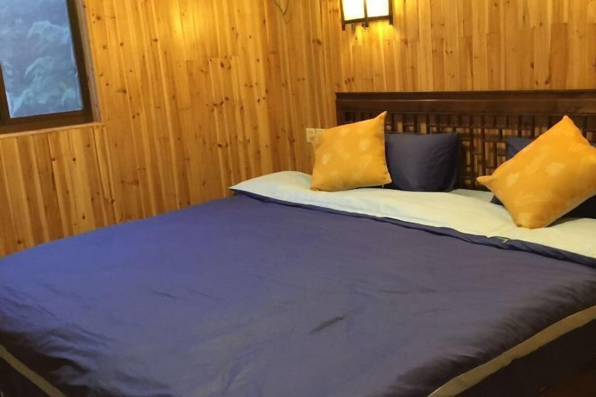 A wooden-paneled room with a bed, two pillows, and a wall-mounted light fixture.