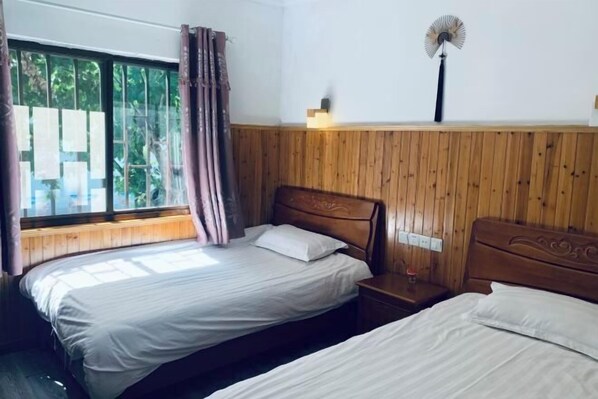 A room with two beds, a wooden wall paneling, a window with curtains, a bedside table, and a wall-mounted fan. - Nanxun One Meter Sunshine Inn (Huzhou)