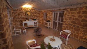 A cozy room with stone walls, a round table, two chairs, a small white desk, and a large mirror. - Teela Jaisalmer Luxury Desert Swiss Tent (Jaisalmer)