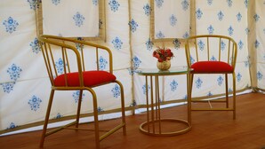 Two chairs with red cushions and a small table with a vase of flowers in a tent-like room with patterned walls. - Teela Jaisalmer Luxury Desert Swiss Tent (Jaisalmer)