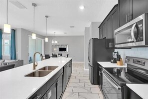 A modern kitchen with stainless steel appliances, a large island with a sink, and a dining area with a view.
