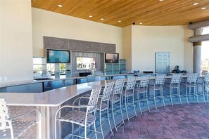 A bar area with a long counter, multiple chairs, and two televisions mounted on the wall.