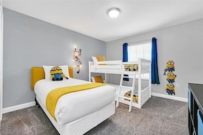 A bedroom with a bunk bed, a desk, and a Minion-themed wall decoration.