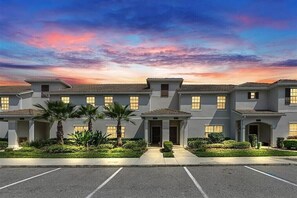 A multi-story building with a symmetrical facade, a central entrance, and a parking lot in front.
