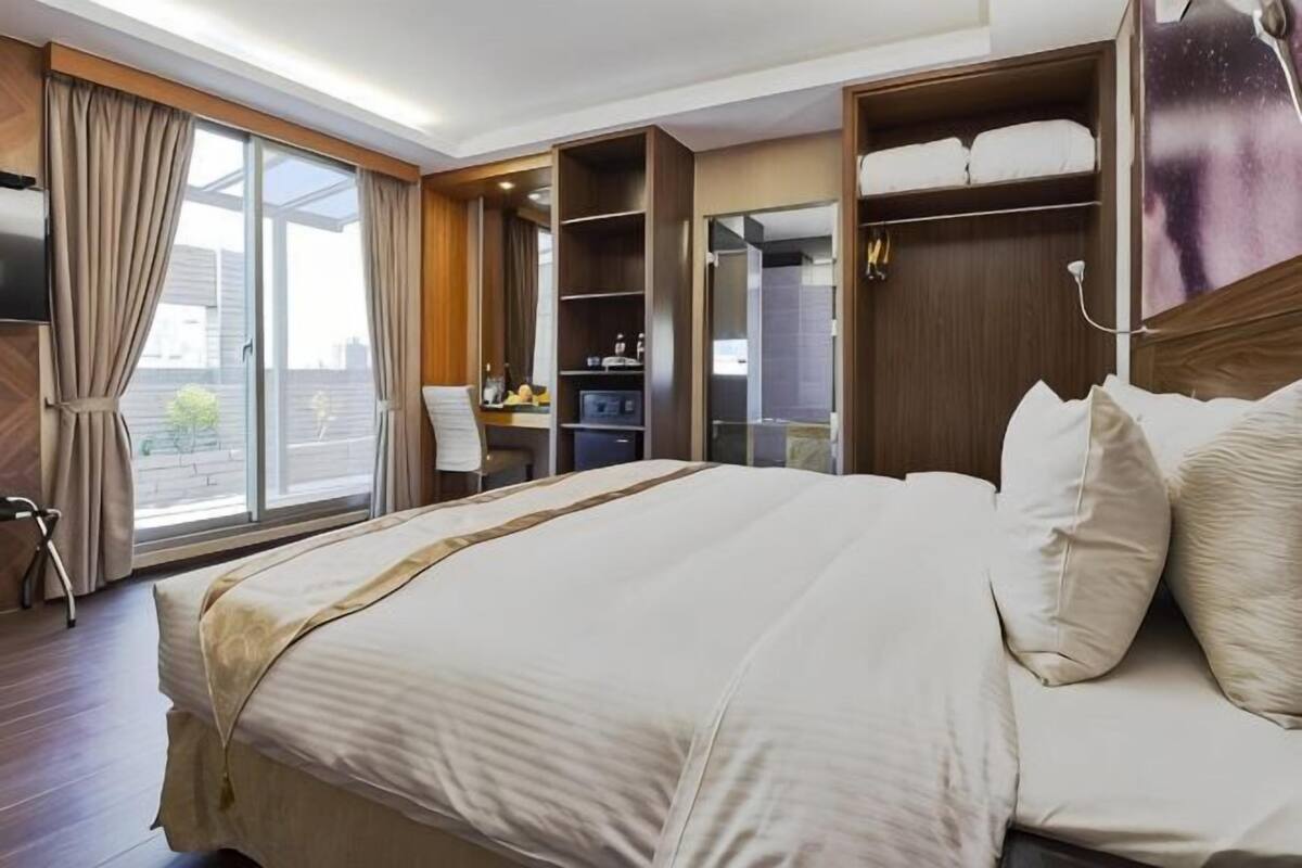 Una habitación de hotel con una cama grande, un escritorio, una silla, un armario y vistas al exterior.