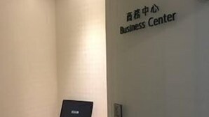 Una habitación con un escritorio, computadora y dos sillas negras. Un cartel en la pared dice 'Business Center'.