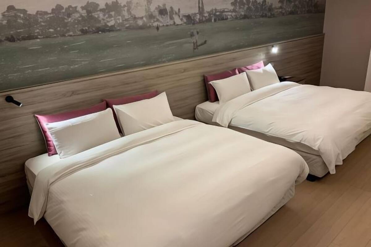 Habitación de hotel con dos camas, un cabecero de madera y un mural con vistas a la ciudad.