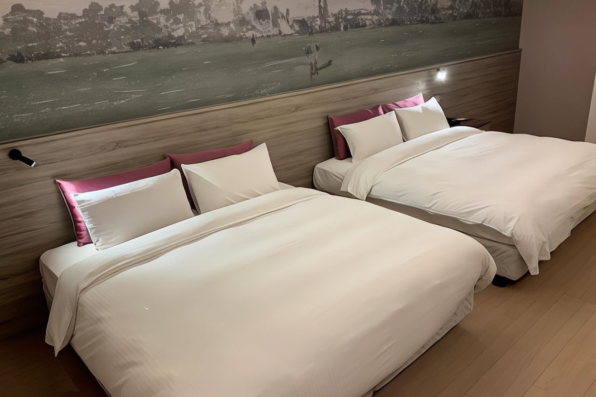 A hotel room with two beds, a wooden headboard, and a cityscape mural on the wall.