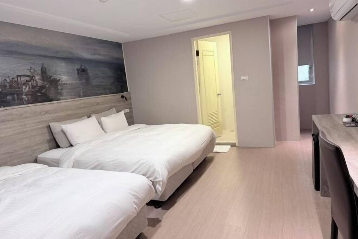 Habitación de hotel con dos camas, un cuadro en la pared, una puerta que da a otra habitación y una mesita pequeña.