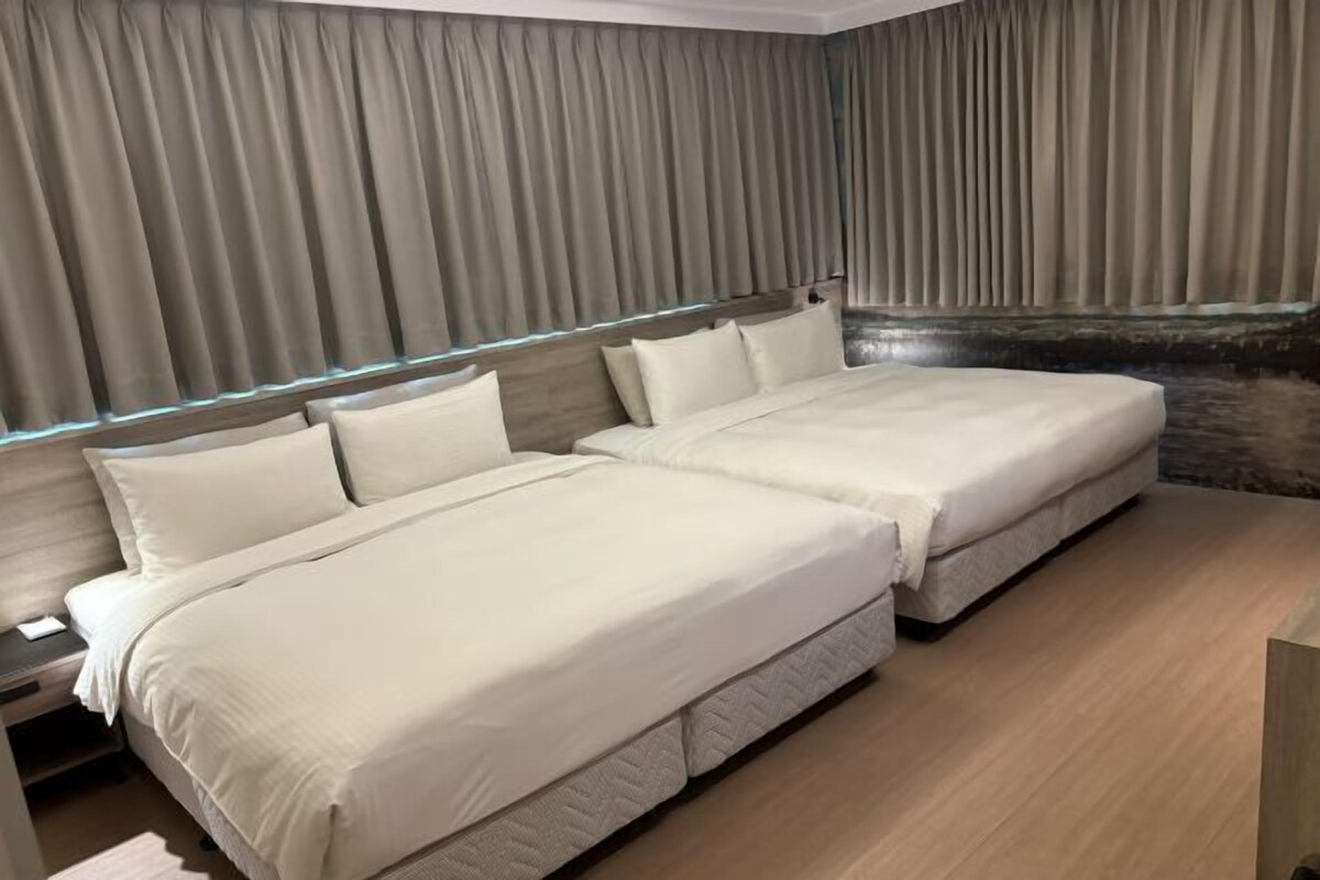 A bedroom with two beds, a wooden headboard, and a large window with curtains.