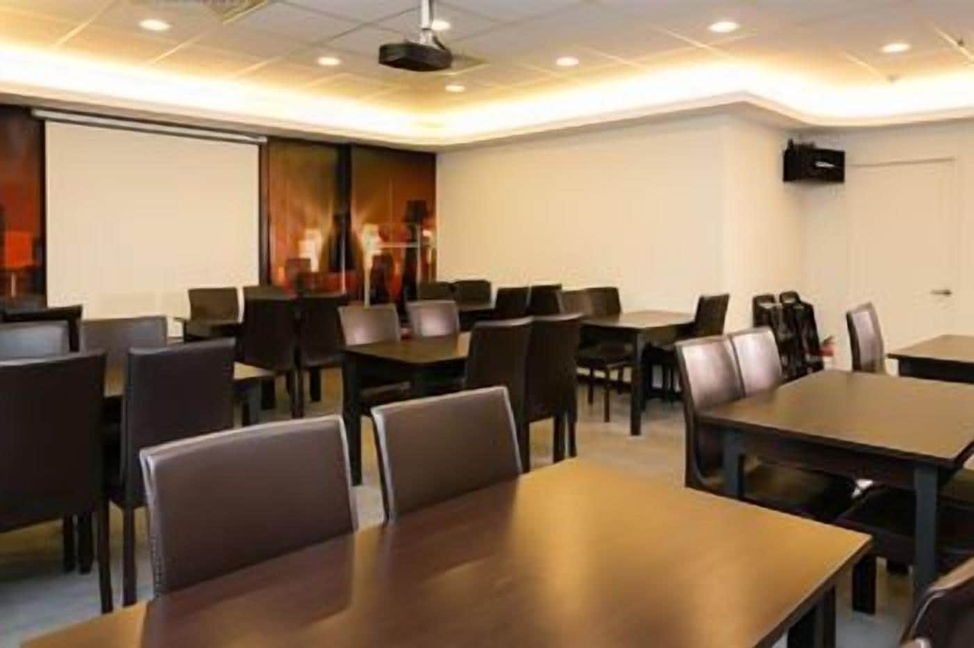A conference room with tables and chairs, a projector screen, and a whiteboard.