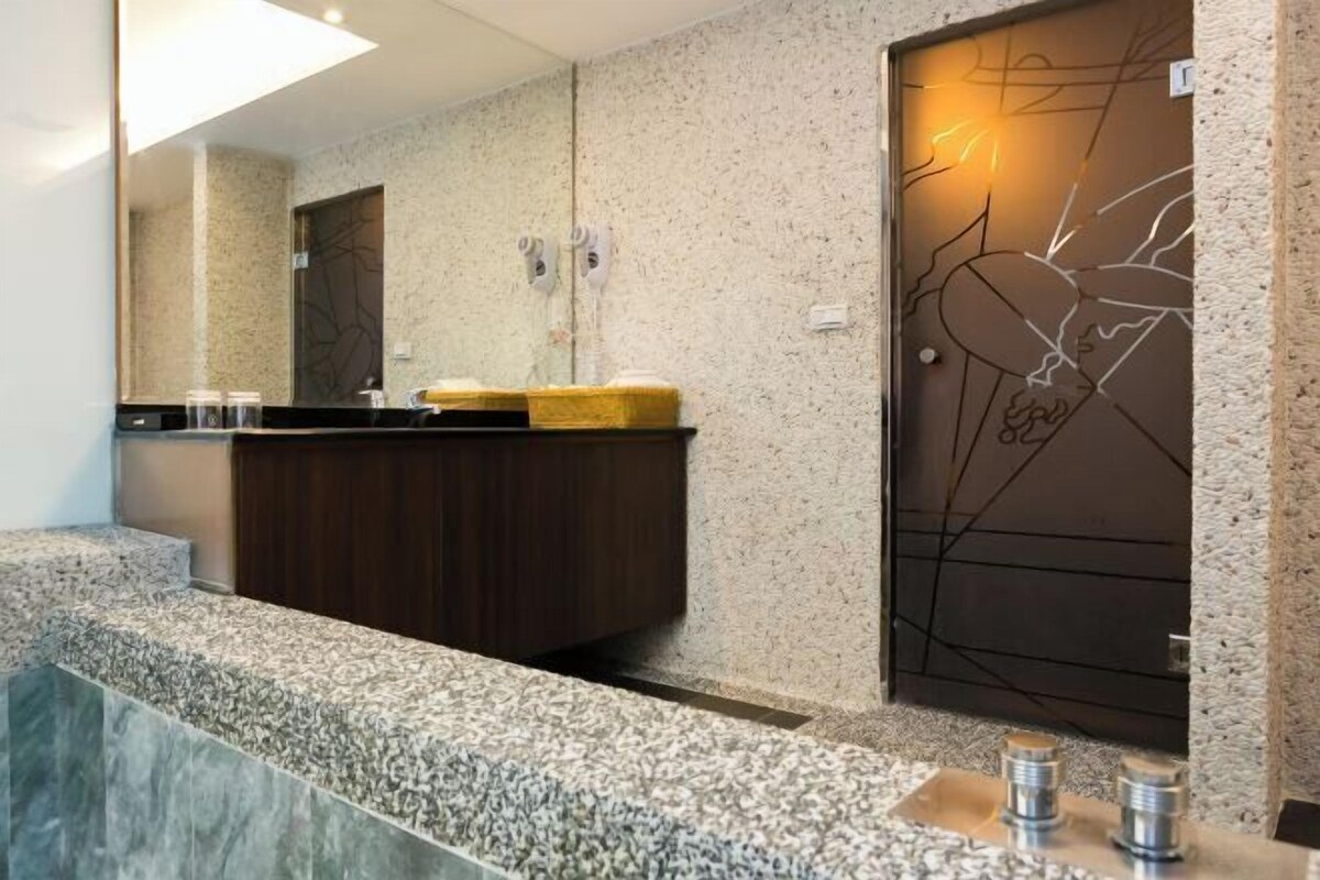 A modern bathroom with a granite countertop, a wooden vanity, and a decorative wall with a light fixture.