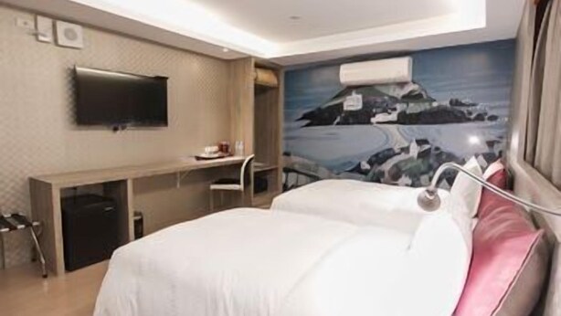 Habitación de hotel con cama, escritorio, silla, televisor y un mural de un paisaje montañoso.