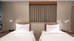 Habitación de hotel con dos camas, una ventana con cortinas, una mesita de noche con teléfono y una pared con textura.