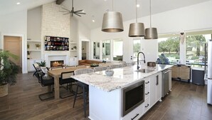 A modern kitchen with a large island, pendant lights, and a stone backsplash.