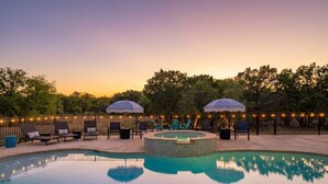 A swimming pool with lounge chairs and umbrellas, surrounded by a fence and trees.
