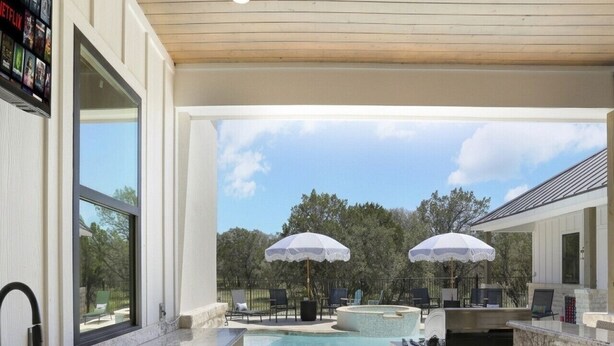 A modern kitchen with a large window, a built-in sink, and a pool area with two umbrellas.